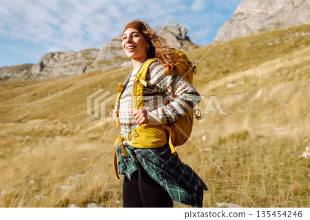 Traveler woman with a bright yellow backpack strolls through golden meadows. Active lifestyle 135454246