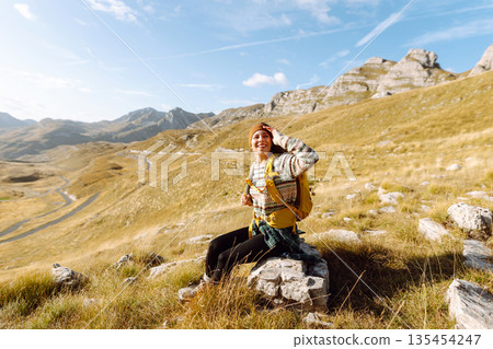 Traveler woman with a bright yellow backpack strolls through golden meadows. Active lifestyle 135454247