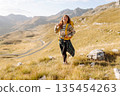 Traveler woman with a bright yellow backpack strolls through golden meadows. Active lifestyle 135454263