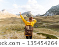 Traveler woman in yellow jacket enjoys hiking on sun. Hiking in mountains with backpacks. Adventure. 135454264