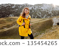 Traveler woman in yellow jacket enjoys hiking on sun. Hiking in mountains with backpacks. Adventure. 135454265