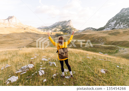 Traveler woman in yellow jacket enjoys hiking on sun. Hiking in mountains with backpacks. Adventure. Traveler woman in yellow jacket enjoys hiking on sun. Hiking in mountains with backpacks. Adventure. 135454266