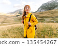 Traveler woman in yellow jacket enjoys hiking on sun. Hiking in mountains with backpacks. Adventure. 135454267