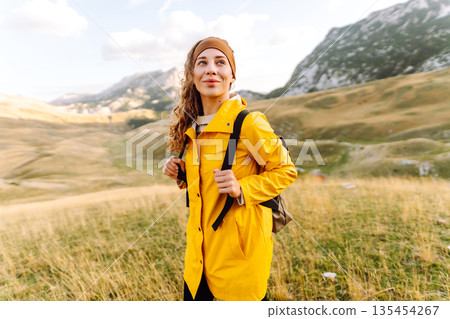 Traveler woman in yellow jacket enjoys hiking on sun. Hiking in mountains with backpacks. Adventure. Traveler woman in yellow jacket enjoys hiking on sun. Hiking in mountains with backpacks. Adventure. 135454267