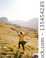 Traveler woman with a bright yellow backpack strolls through golden meadows. Active lifestyle 135454285