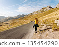 Hitchhiking woman traveler try to stop car on the mountain road. Travel and vacation theme 135454290