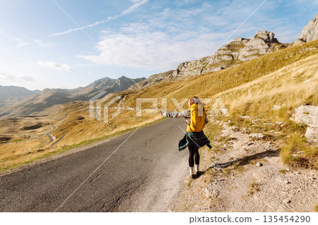 Hitchhiking woman traveler try to stop car on the mountain road. Travel and vacation theme 135454290