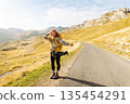 Hitchhiking woman traveler try to stop car on the mountain road. Travel and vacation theme 135454291