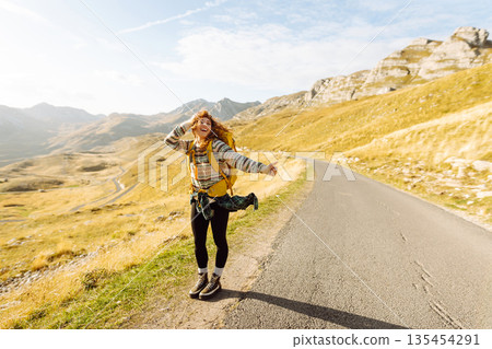 Hitchhiking woman traveler try to stop car on the mountain road. Travel and vacation theme 135454291