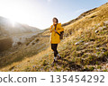 Traveler woman in yellow jacket enjoys hiking on sun. Hiking in mountains with backpacks. Adventure. 135454292