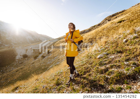 Traveler woman in yellow jacket enjoys hiking on sun. Hiking in mountains with backpacks. Adventure. 135454292