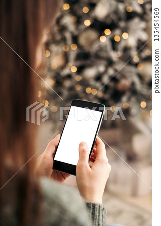 christmas mockup with space for text. christmas advertising, app template. hands holding phone with empty screen on background of beautiful christmas tree with lights christmas mockup with space for text. christmas advertising, app template. hands holding phone with empty screen on background of beautiful christmas tree with lights 135454569