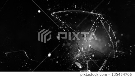 Front view photo of glass shattered by a bullet. Gunshot impact creates cracks, flying shards and dust isolated on black background. Perfect VFX overlay element or dramatic background. Front view photo of glass shattered by a bullet. Gunshot impact creates cracks, flying shards and dust isolated on black background. Perfect VFX overlay element or dramatic background. 135454706