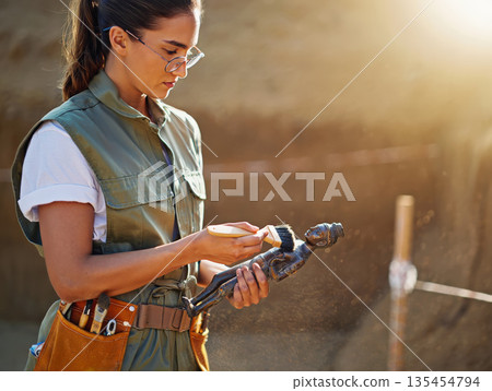 Female archaeologist carefully cleans an ancient figurine found at an archaeology site. Young woman uses a fine brush to remove dust from a old artifact. Discovery and historical preservation concept 135454794