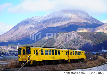 A lightly snow-covered Mount Yufu and a yellow diesel train A lightly snow-covered Mount Yufu and a yellow diesel train 135454822