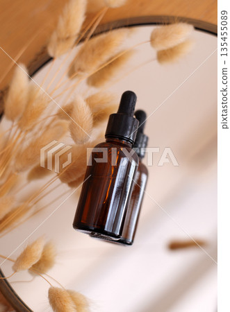 Amber glass dropper bottle reflected in a mirror with dried fluffy grass. Aesthetic skincare or essential oil concept. 135455089