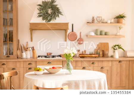 Cozy rustic kitchen interior with wooden cabinets, dining table, white tulips, and warm farmhouse decor. Cozy rustic kitchen interior with wooden cabinets, dining table, white tulips, and warm farmhouse decor. 135455384