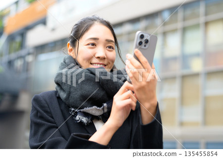 A woman wearing a scarf using a smartphone A woman wearing a scarf using a smartphone 135455854