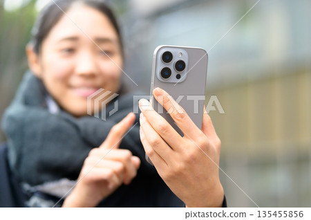一位戴著圍巾的女士正在使用智慧型手機 135455856