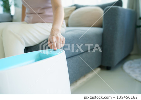 Woman using home air purifier or humidifier in living room. Woman using home air purifier or humidifier in living room. 135456162
