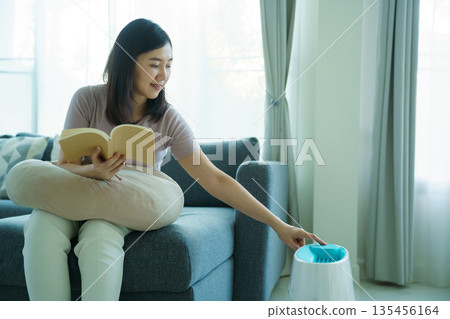 Woman using home air purifier or humidifier in living room. Woman using home air purifier or humidifier in living room. 135456164