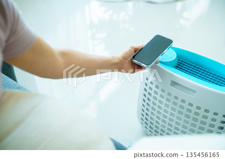 Woman controlling home air purifier or humidifier with smartphone while relaxing at home. Woman controlling home air purifier or humidifier with smartphone while relaxing at home. 135456165