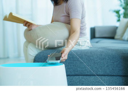 Woman controlling home air purifier or humidifier with smartphone while relaxing at home. 135456166
