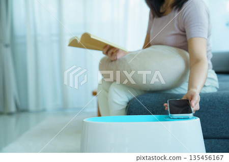 Woman controlling home air purifier or humidifier with smartphone while relaxing at home. Woman controlling home air purifier or humidifier with smartphone while relaxing at home. 135456167