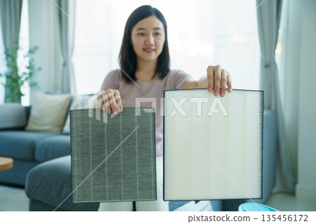 Asian woman showing dirty and clean air purifier filters for comparison. 135456172