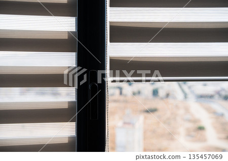 Modern zebra roller blinds on apartment window with soft daylight filtering and blurred cityscape background 135457069
