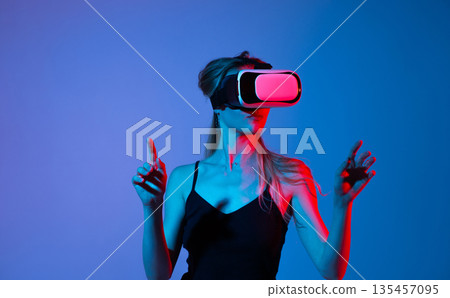 Woman adjusting virtual reality headset in blue light studio, immersive VR technology, modern innovation and digital experience Woman adjusting virtual reality headset in blue light studio, immersive VR technology, modern innovation and digital experience 135457095