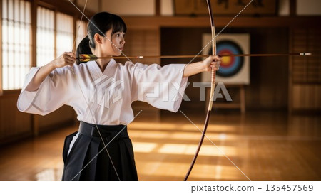 A female high school student quietly draws a bow while looking at the target at the archery field 135457569