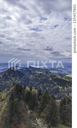 Forested hills stretch toward the horizon under a cloudy sky, with distant valleys and water barely visible. Forested hills stretch toward the horizon under a cloudy sky, with distant valleys and water barely visible. 135457601
