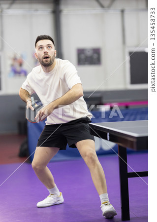 Young man playing table tennis during intense match Young man playing table tennis during intense match 135458733