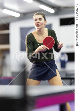 Woman playing table tennis holding paddle and ball 135458767
