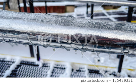 Close-up of frozen metal railings covered in thick ice and small icicles on a cold winter day. 135459331