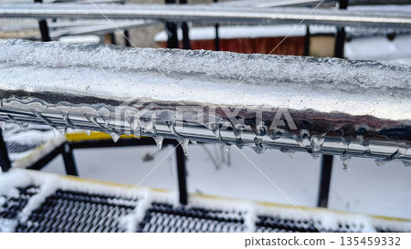 Close-up of frozen metal railings covered in thick ice and small icicles on a cold winter day. 135459332