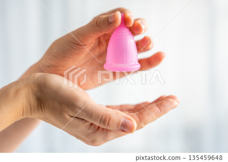 Hands gently holding a pink menstrual cup, symbolizing care, protection, and sustainable feminine hygiene. Concept of eco-friendly period product and body positivity. 135459648