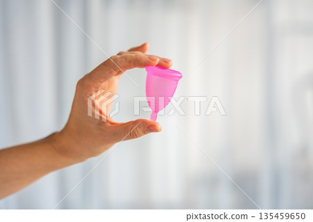 Close-up of a pink menstrual cup standing upright on a woman open palm over wooden table. Feminine hygiene product promoting zero waste, comfort, and sustainable period care. 135459650