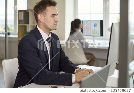 Focused businessman typing at desktop computer in modern light office workspace Focused businessman typing at desktop computer in modern light office workspace 135459657