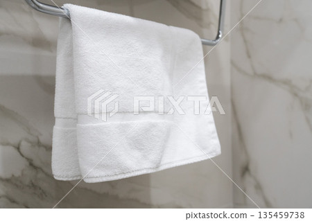 Clean white towel hanging on a chrome towel rail against a marble bathroom wall, minimalist hotel interior detail Clean white towel hanging on a chrome towel rail against a marble bathroom wall, minimalist hotel interior detail 135459738