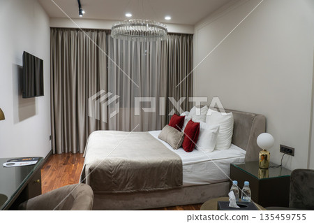 Modern hotel bedroom with double bed, decorative pillows, bedside lamp, bottled water, floor-to-ceiling curtains, designed in contemporary style Modern hotel bedroom with double bed, decorative pillows, bedside lamp, bottled water, floor-to-ceiling curtains, designed in contemporary style 135459755
