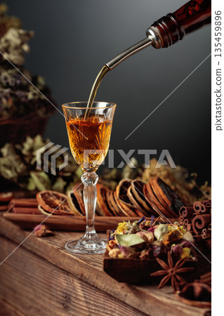Herbal liquor is poured from a vintage bottle into a glass. 135459896