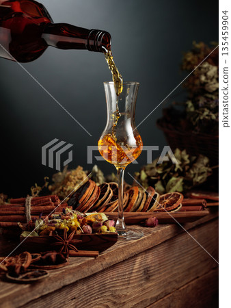 Herbal liquor is poured from a vintage bottle into a glass. Herbal liquor is poured from a vintage bottle into a glass. 135459904
