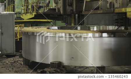 Factory worker operates large lathe machine, producing metal ring. Stock clip 135460243