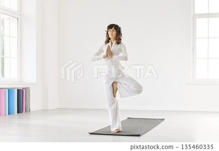 Graceful tree pose practice: woman balancing on yoga mat in bright studio 135460335