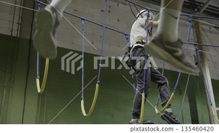 Adventurous man carefully crossing rope bridge in indoor climbing gym. Creative 135460420