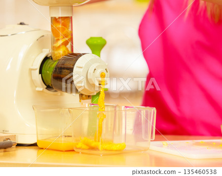 Making orange juice in juicer machine in kitchen 135460538