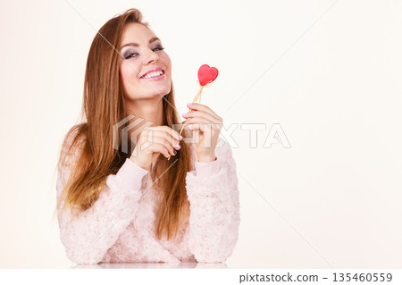 Flirty woman holding red wooden heart on stick Flirty woman holding red wooden heart on stick 135460559