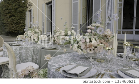 Elegant wedding reception table setting with floral centerpiece in a villa garden. Action Elegant wedding reception table setting with floral centerpiece in a villa garden. Action 135460621